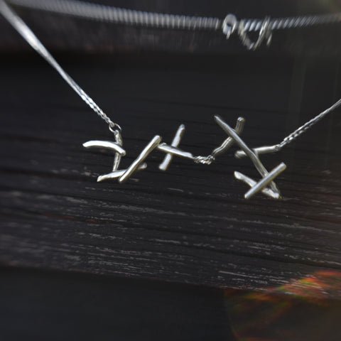 Yöpiikki Necklace,  handmade jagged thorn necklace in recycled sterling silver. Here photographed on a dark wood background.