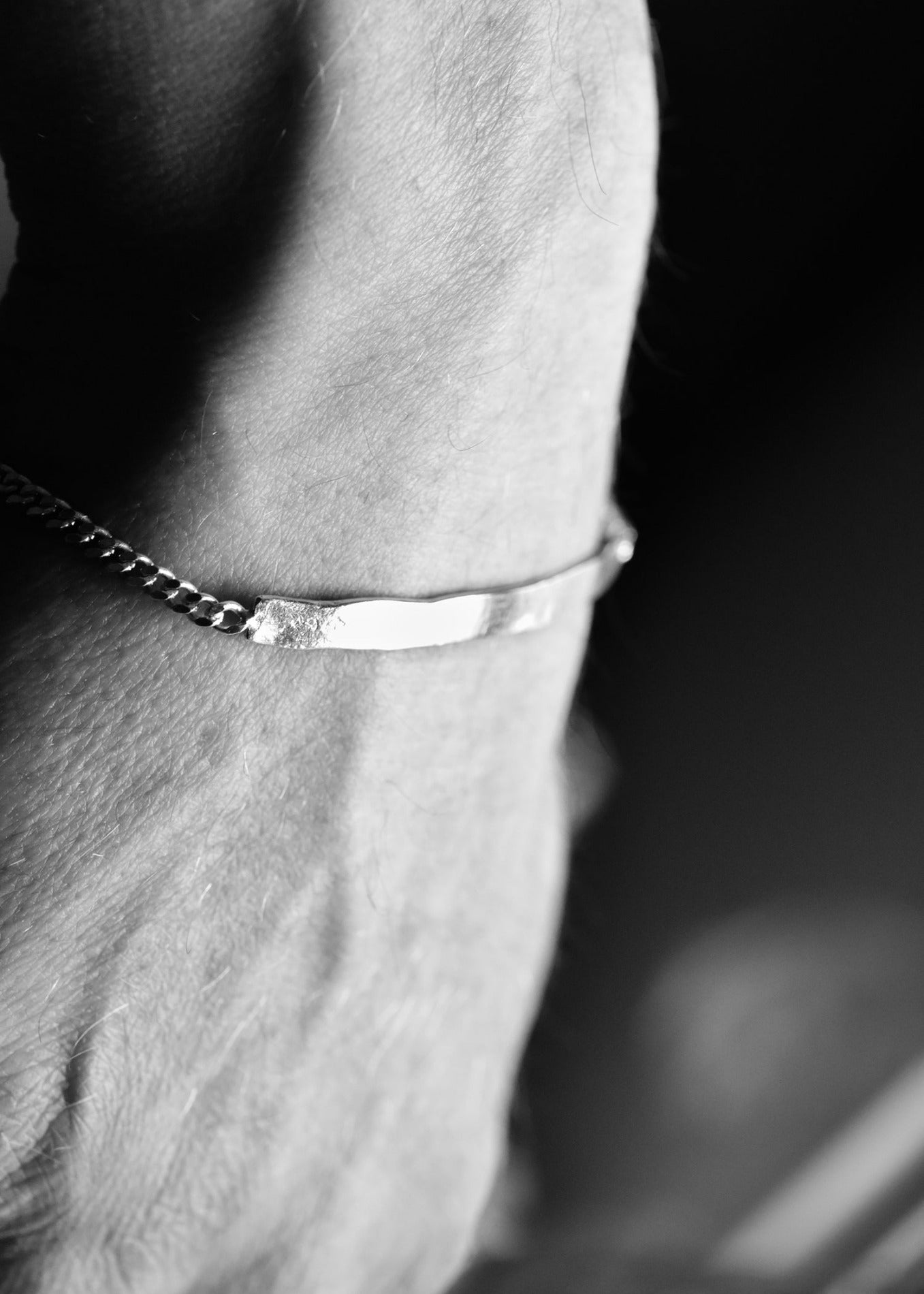 Close-up of a person's arm wearing a silver bracelet against a dark background