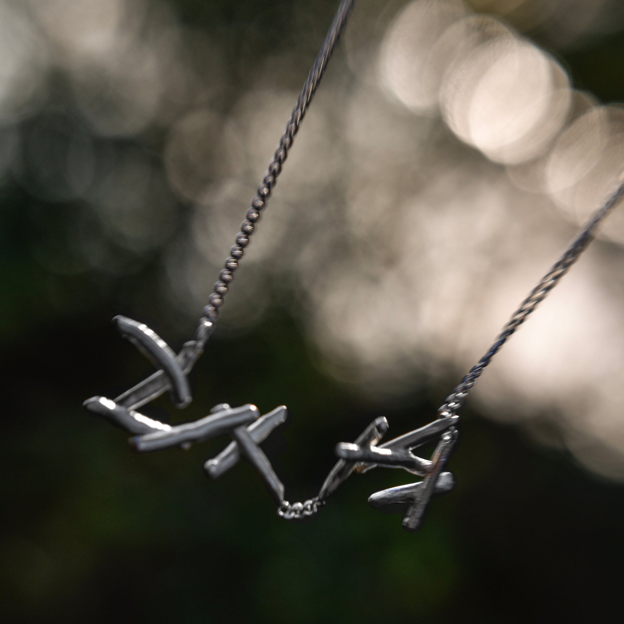Sterling Silver necklace and a pendant, photographed against a blurred dark green and black outdoor background.
