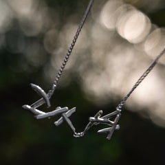 Sterling Silver necklace and a pendant, photographed against a blurred dark green and black outdoor background.